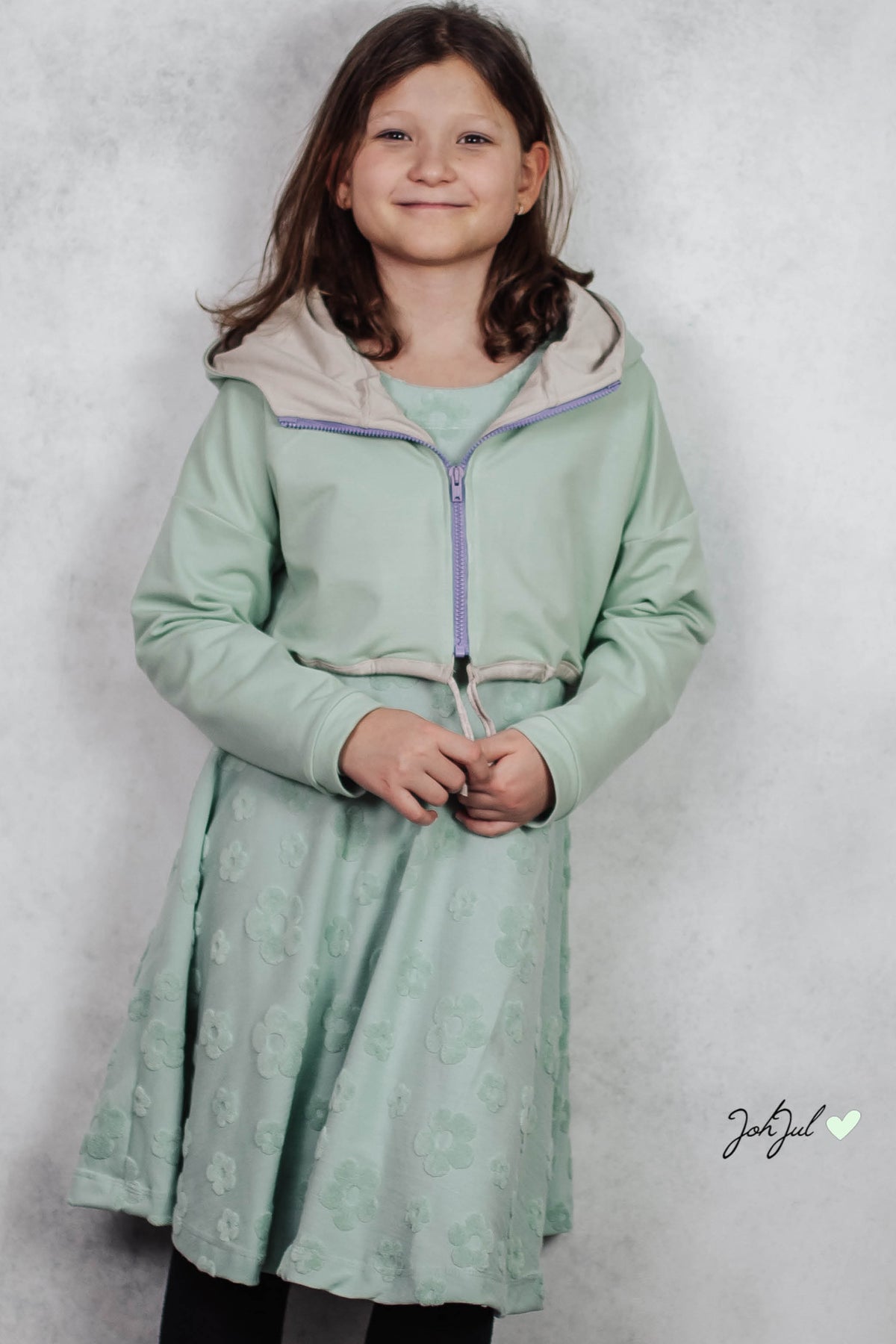 Kurze mintfarbene Macadamia-Jacke mit hell gefütterter Kapuze und Reißverschluss über einem passenden Kleid